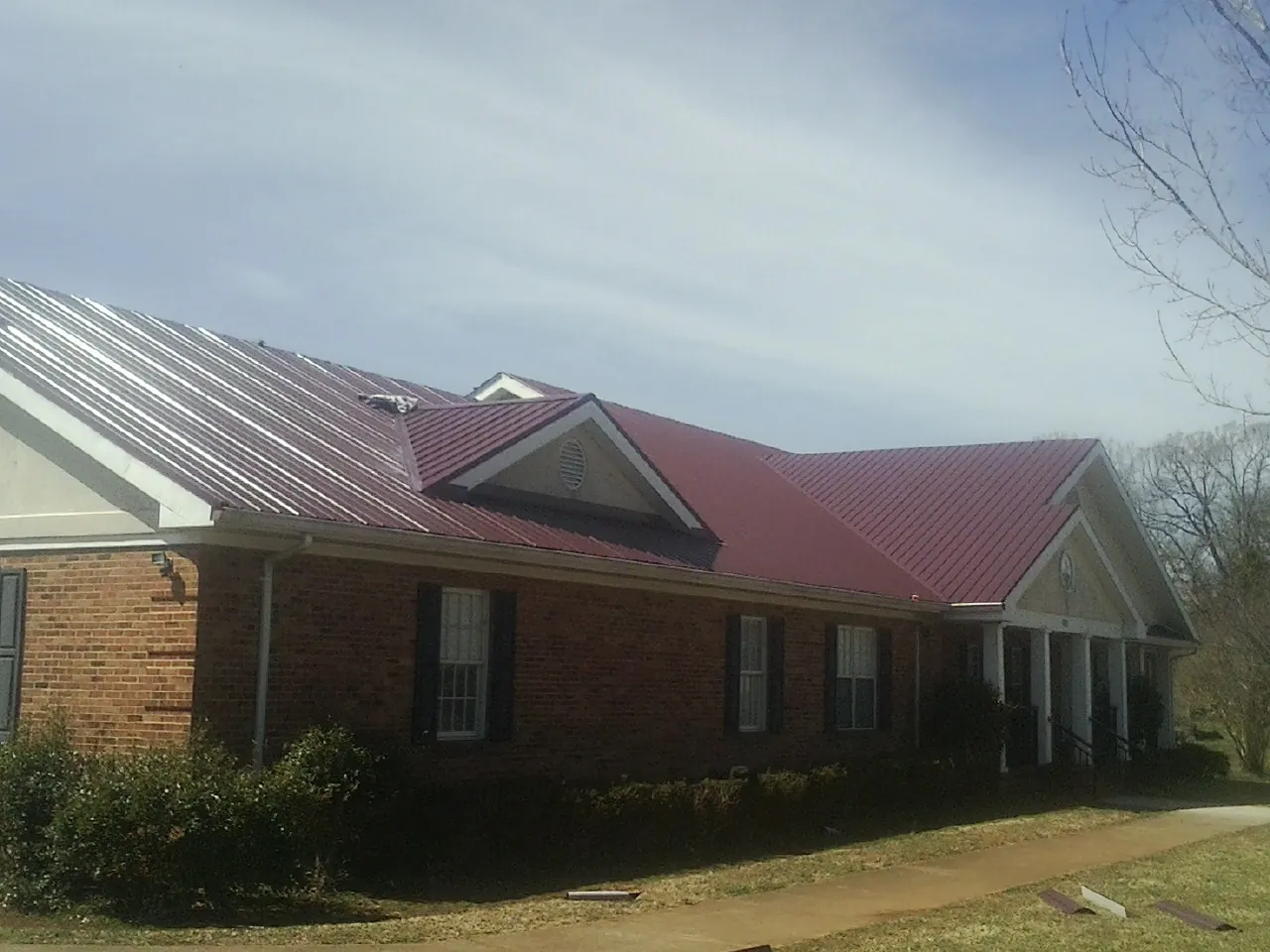 Red metal roof with gabled entries on a long brick building, from a Hail Damage Roof Repair job in Milledgeville
